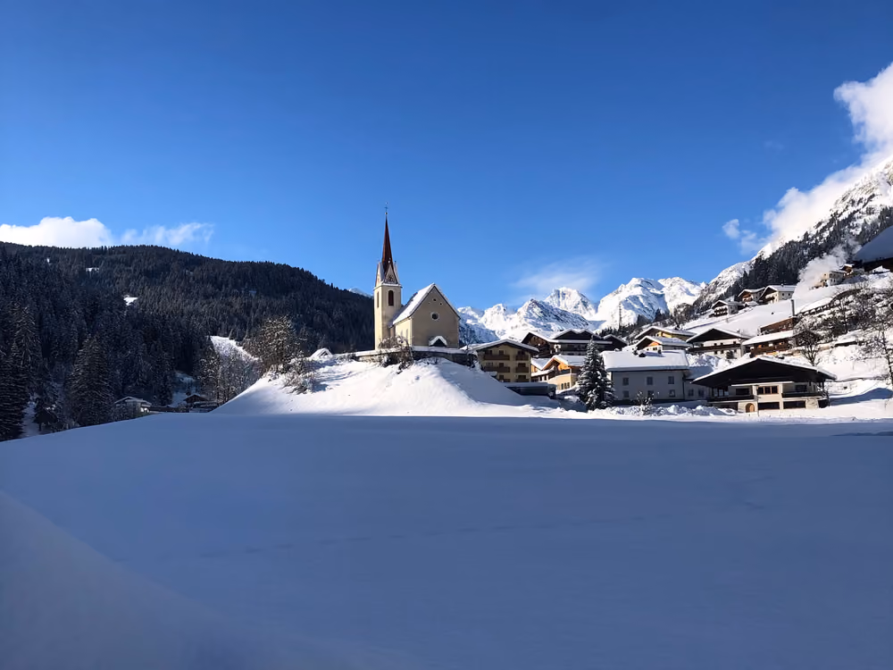 Verschneites Ratschings mit Kirchturm, Höfen und Bergpanorama